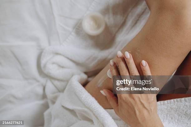 a woman hands applies moisturizing or anti-cellulite or anti-aging cream to the skin of her thighs, daily skin care after a shower - anti age stock-fotos und bilder