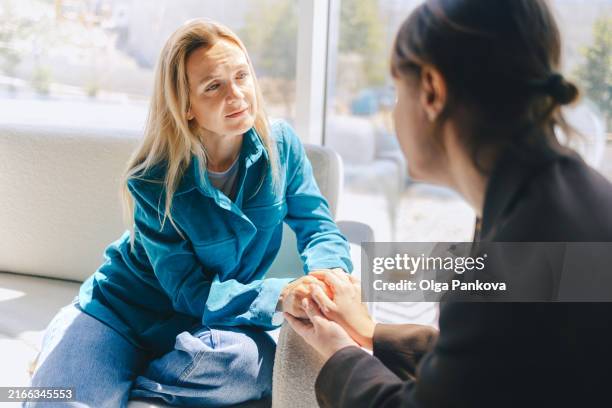 two middle-aged women hold each other's hands as a sign of support and empathy. office, colleagues, joint problem solving. - empatia foto e immagini stock