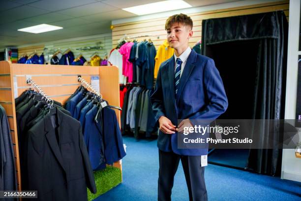 hijo adolescente comprando ropa nueva para la escuela, probándose un uniforme escolar - uniforme de colegio fotografías e imágenes de stock