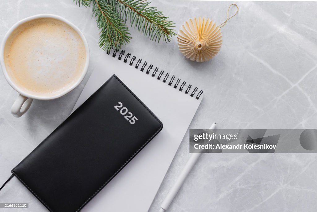 Diary for the year 2025, note pad, cup of coffee and spruce branch on table. New year planning concept