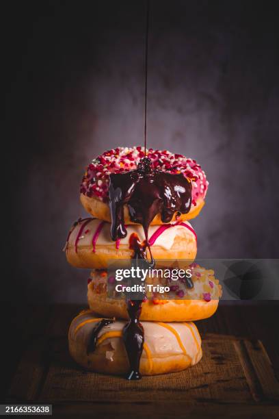 close-up of coloured doughnuts dripping liquid chocolate on them with natural light coming in from the right and dark background, copy space - glassa foto e immagini stock