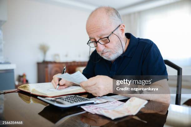 anxious senior man managing finances, holding cash and using calculator at home - pensão documento bancário imagens e fotografias de stock