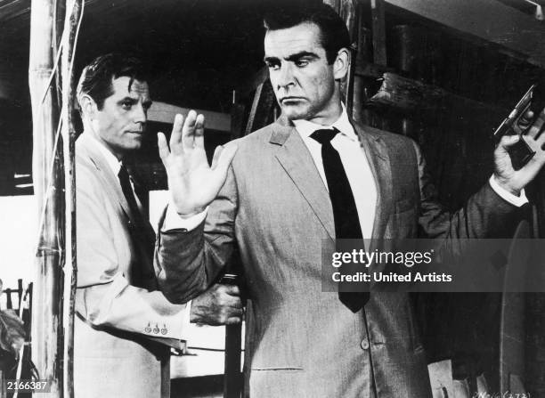 Jack Lord hold Sean Connery at gunpoint in a still from the James Bond film, 'Dr. No,' directed by Terence Young, 1962.