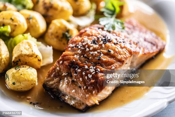 crispy baked salmon fillet sprinkled with sesame with young potatoes and demiglas sauce on a white plate. - gergelim - fotografias e filmes do acervo