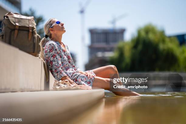 woman enjoying break on sunny summer day during a heat wave at city pond - hittegolf stockfoto's en -beelden
