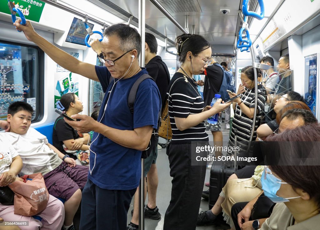 Passengers look at their mobile phones while riding the...