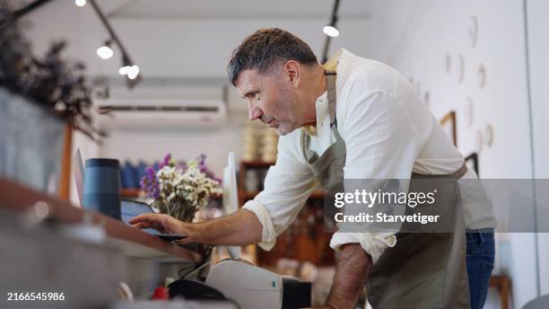 leitender kleinunternehmer, der in seinem einzelhandelsgeschäft inventur durchführt, indem er den laptop zum arrangieren und zusammenfassen von daten für das ziel verwendet, den mindestbestand für die bestandstheorie des managementbestands zu ermitteln - renovierung themengebiet stock-fotos und bilder