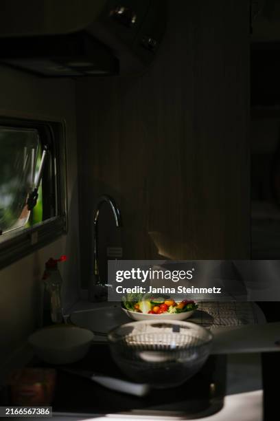 past out-of-focus kitchen appliances to a plate full of vegetables standing in the half-shade in the kitchen of a mobile home - salatschüssel stock-fotos und bilder