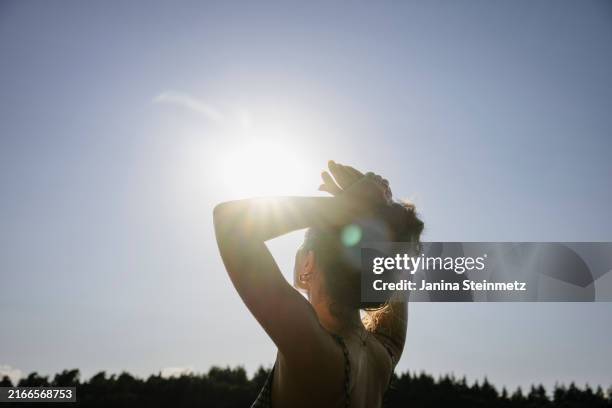 sunlight shines into the camera while a woman looks up at the sky - luce solare foto e immagini stock