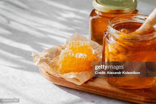 honeycomb and two glass jars with honey. fresh organic honey on white table background with shadow sunlight. copy space - miel photos et images de collection