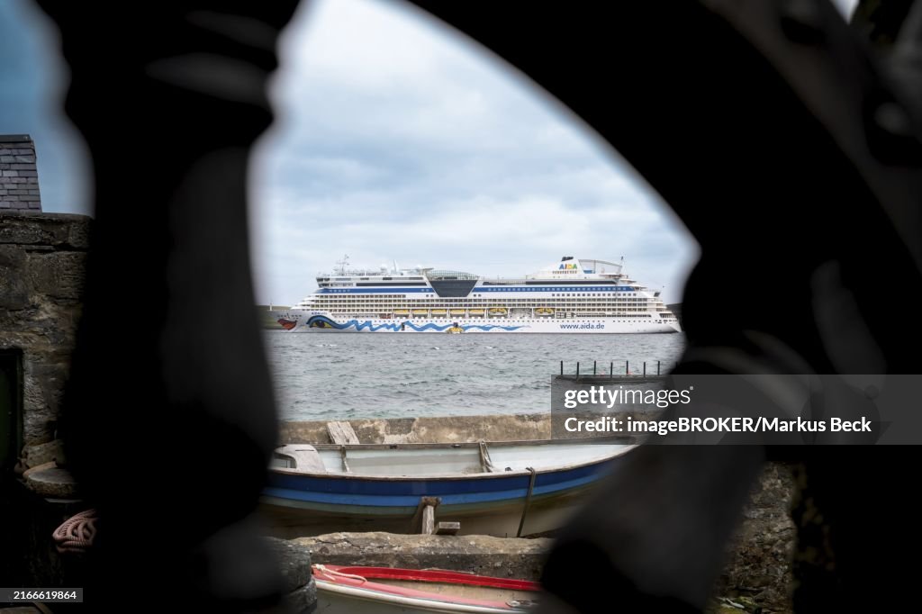 AIDA Bella cruise ship view through wooden wheel anchored in Scotland with small ship in front