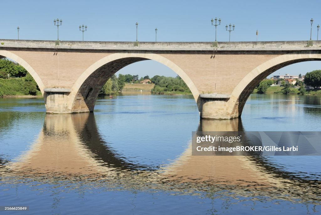A stone bridge with arches reflecting in a calm river under a clear blue sky, Bergerac Dordogne