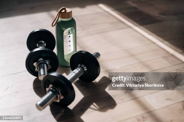 close up of dumbbells and water bottle on the yoga mat in a fitness center, home gym background with space for copy - fitnessapparatuur stockfoto's en -beelden