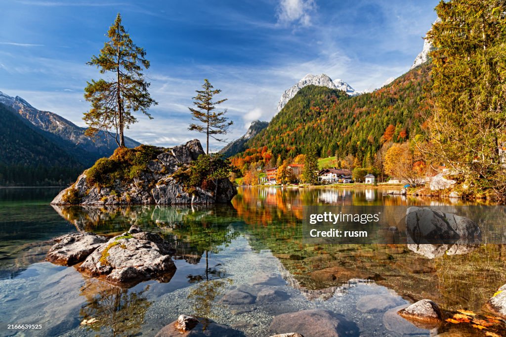 Small island reflected in calm Hintersee lake at clear autumn morning, Berchtesgaden park, Germany.