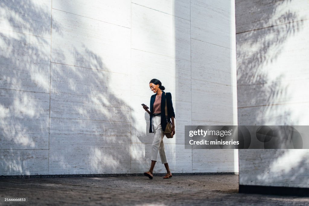 Femme d’affaires noire marchant dans la ville avec un smartphone