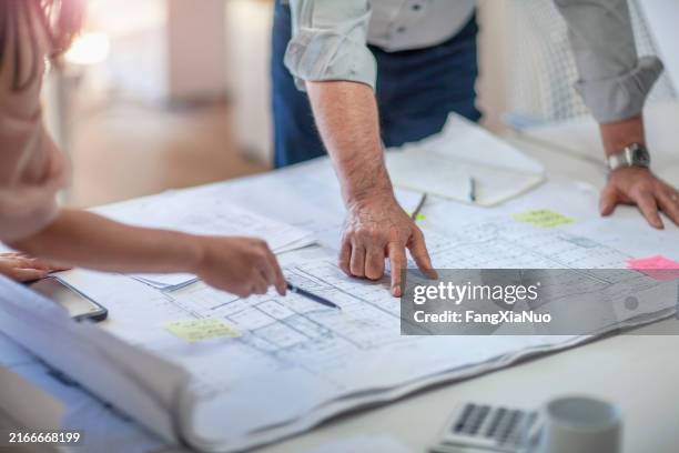colleagues gesturing pointing at architectural plans on tabletop desk in office - blauwdruk stockfoto's en -beelden