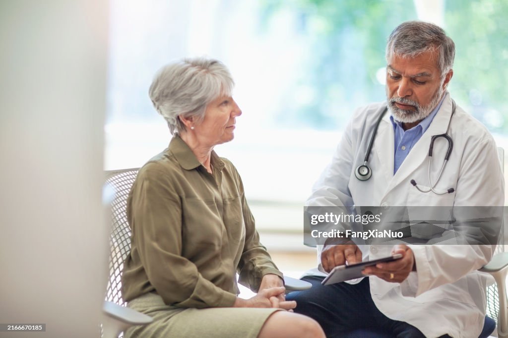 Asiatischer Inder, Pazifikinsulaner, leitender Mann, Arzt, medizinischer Fachmann, spricht mit digitalem Tablet mit Seniorin in Gesundheitsklinik