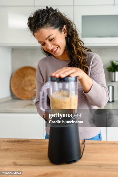 woman preparing a smoothie in her kitchen at home - liquidiser stock pictures, royalty-free photos & images