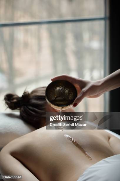 professional applies warm aroma oil to a client's back in a calming spa environment, promoting relaxation and skin care. - health spa stock pictures, royalty-free photos & images