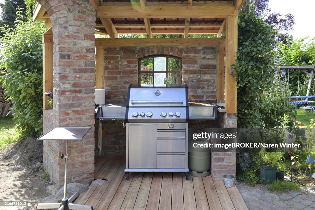 Modern steel gas grill in a shelter made of old bricks and wood, concept for barbecue and garden design, selected focus