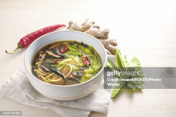 spicy asian vegetable soup with noodles, miso, nori seaweed, ginger and chili in a bowl on a wooden table, copy space, selected focus, narrow depth of field - bouillon photos et images de collection