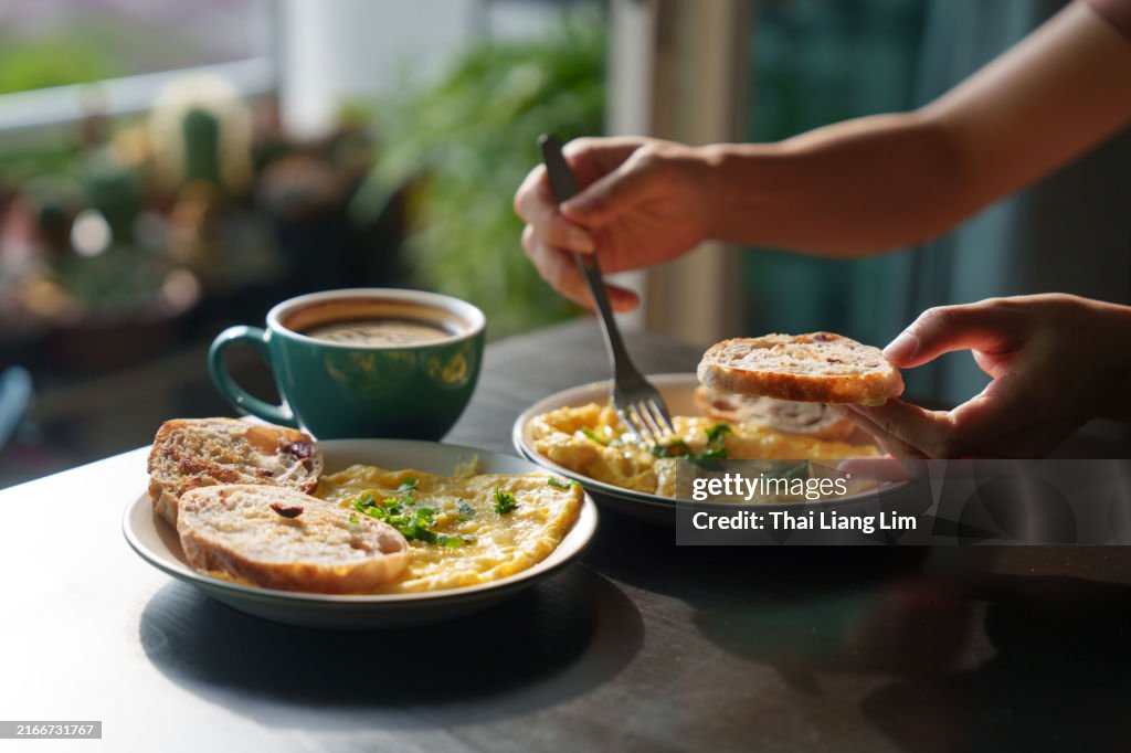 Ein ausgeschnittenes Bild einer Frau, die ein Stück geröstetes Brot mit Rührei darauf hält, während sie morgens ein gesundes Frühstück genießt