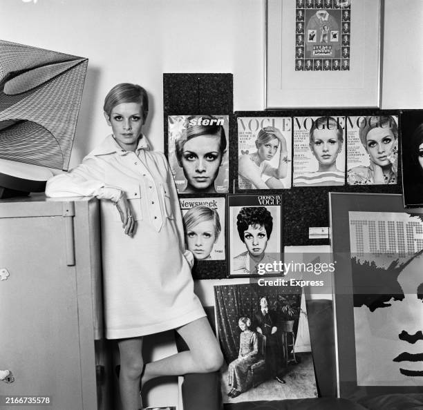 Fashion model Twiggy wearing a shirt dress from her own collection while standing in front of a display of press photographs and Vogue magazine...