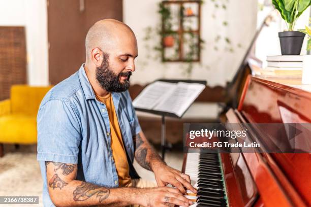 mid adult man playing piano at home - man playing piano stock pictures, royalty-free photos & images