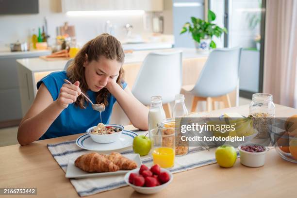 upset and sad adolescent girl sitting at table eating breakfast cereal - met de kop tegen de muur lopen stockfoto's en -beelden