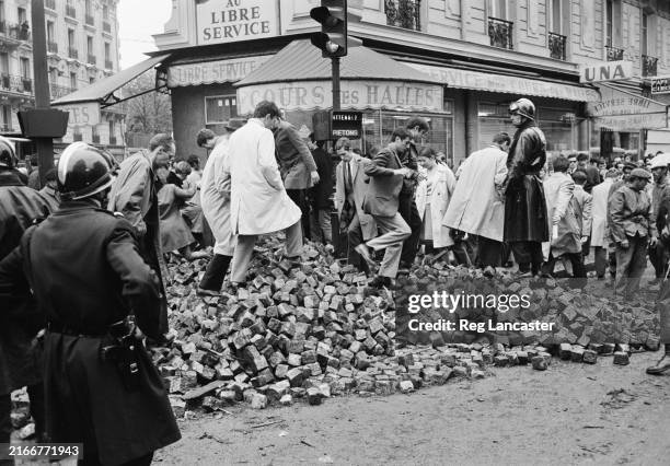 Pedestrians walk over a pile of bricks in the aftermath of the student riots, Paris, France, May 13th 1968.