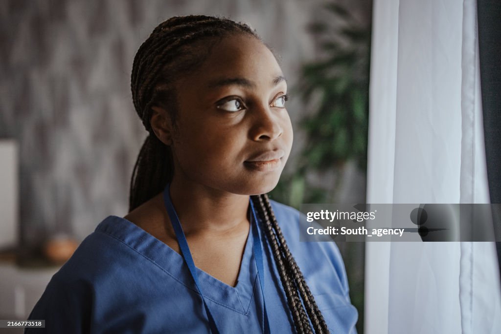 Person in scrubs standing by window in stylish room.