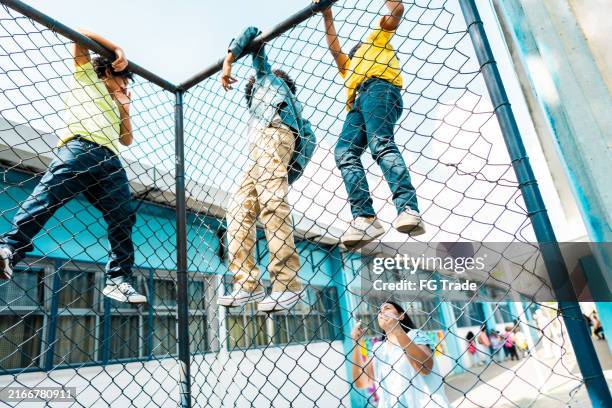 teacher scolding with students climbing on chainlink fence on schoolyard - spielregeln stock-fotos und bilder
