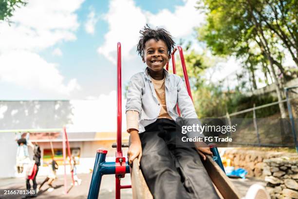 portrait of a schoolboy playing on slide on school playground - south american people stock pictures, royalty-free photos & images