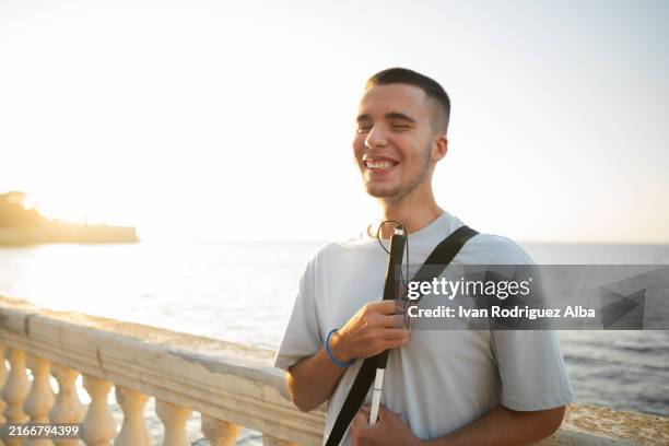 blind person smiling holding white cane by sea at sunset - glaucoma awareness stock pictures, royalty-free photos & images