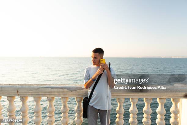 blind person using smartphone app for orientation and accessibility at seafront - blindheid stockfoto's en -beelden