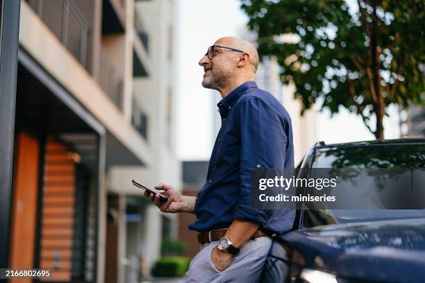 businessman leaning on car in urban city environment - levantador imagens e fotografias de stock