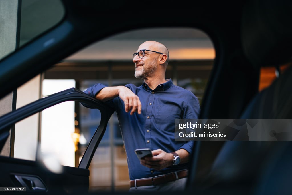 Confident Businessman Standing by Car with Smartphone in City