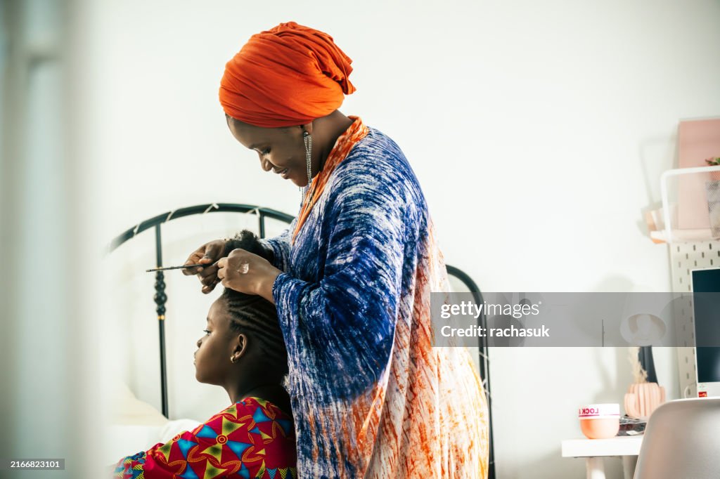 Mirror reflection of Black girl gets her hair braided by mother