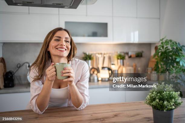 una joven disfruta de su cocina, vestida con un pijama, bebiendo su café matutino - chica-tomando-cafe fotografías e imágenes de stock
