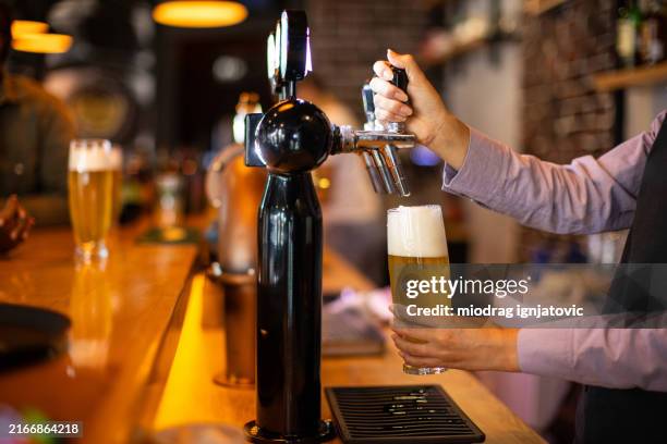 bartender pouring beer from a tap into glasses - gieten stockfoto's en -beelden