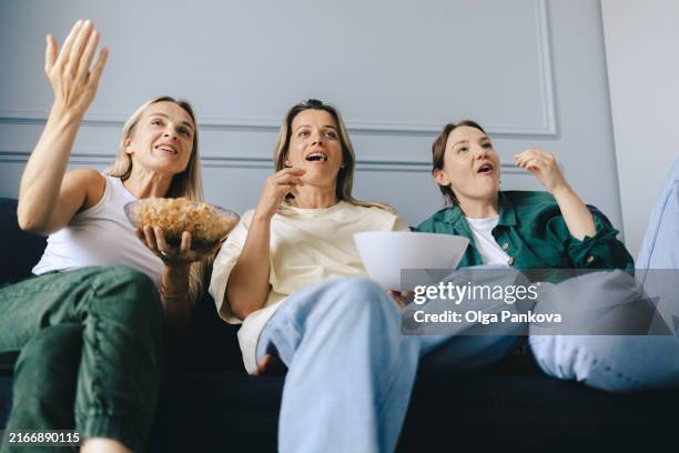 female friends spend time at home watching soccer and eating popcorn - fan with colored streamers stock pictures, royalty-free photos & images