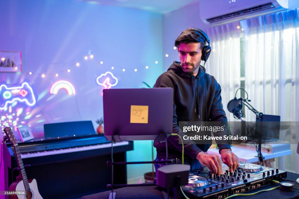 Caucasian young man artist DJ mixing and scratching music mixer controller. Attractive male musician DJ having fun mixing music on console touching buttons and playing electronic music at neon party.