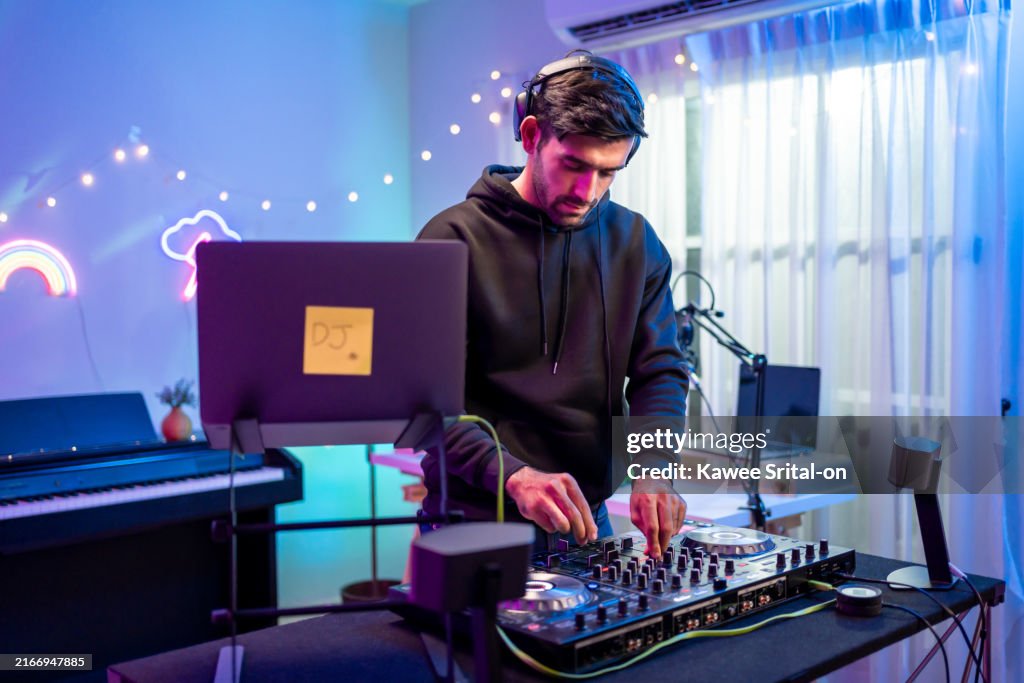 Caucasian young man artist DJ mixing and scratching music mixer controller. Attractive male musician DJ having fun mixing music on console touching buttons and playing electronic music at neon party.