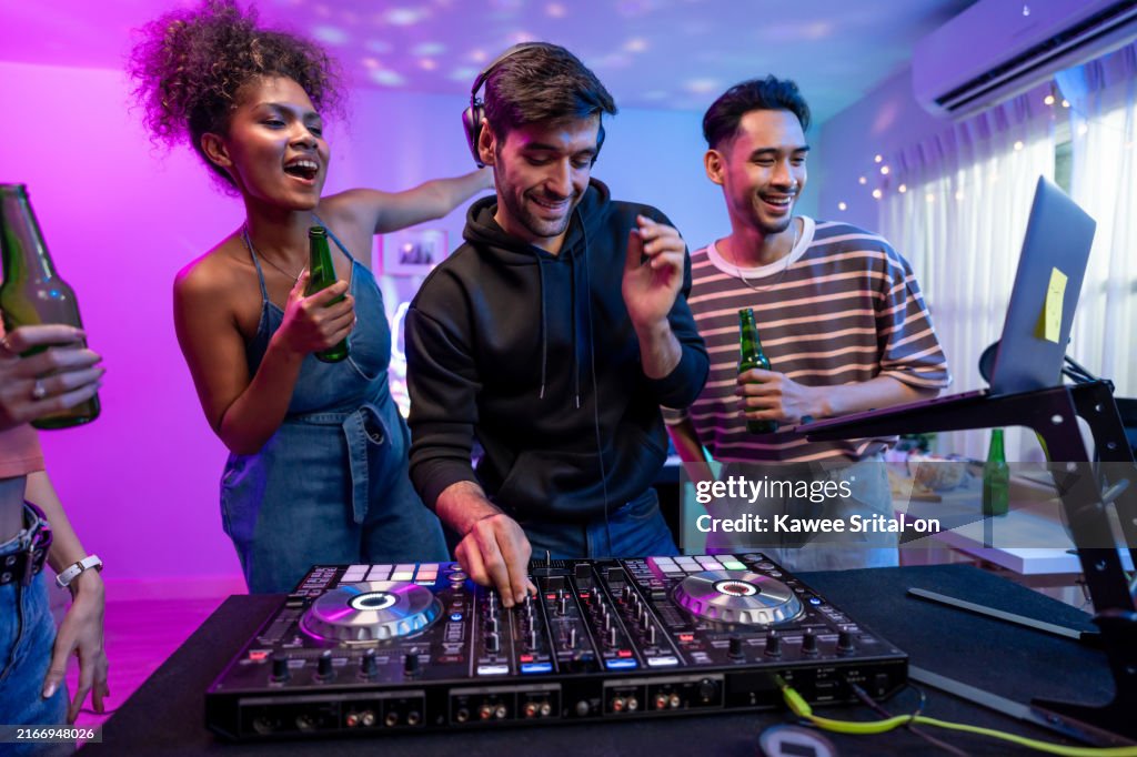 Group of diverse man and woman dancing with DJ mixing music on console. Attractive young teenager friends having fun with DJ mixing and scratching music mixer controller at house party with neon light