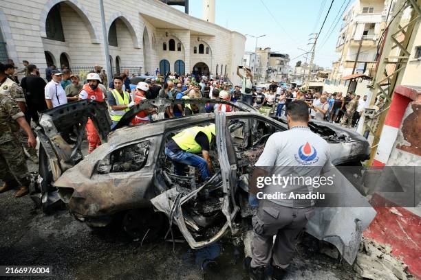 Emergency teams and civilians are seen around a car which was left unusable after an Israeli army unmanned aerial vehicle attack which killed one...