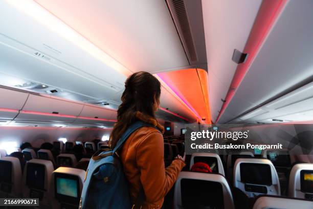 a woman boards a small commercial airplane, carrying a backpack. she walking the aisle on plane - einsteigen stock-fotos und bilder