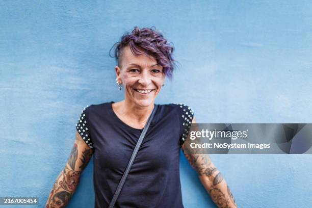 smiling woman with tattoos against blue wall - new wave stock pictures, royalty-free photos & images