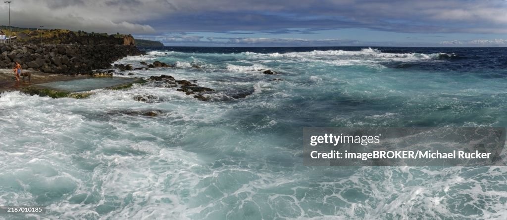 Stormy waves crash against a rocky shore under a cloudy sky, seawater bathing establishment, Capelas, Sao Miguel Island, Azores, Portugal, Europe