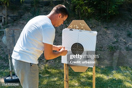 Mid-Adult Man Counting The Score After Shooting A Target With A In An Outdoor Shooting Range Mid-Adult Man Counting The Score After Shooting A Target With A In An Outdoor Shooting Range