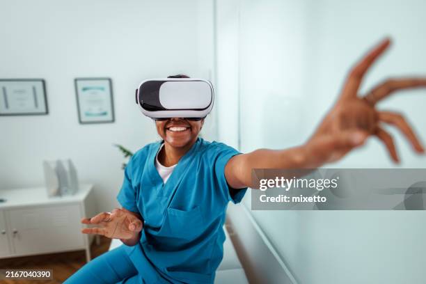 cheerful young female doctor using vr goggles while sitting at doctor's office - virtual reality stockfoto's en -beelden